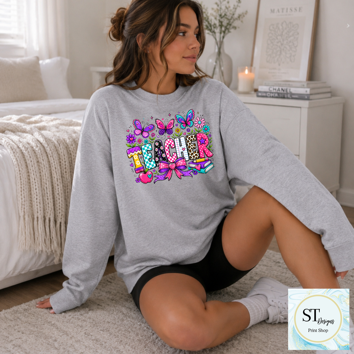 Colorful teacher graphic crewneck sweatshirt in sand color, featuring vibrant educational-themed design from ST Designs Store.