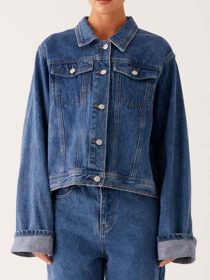 Dark blue oversized denim jacket with button-down front, cropped style, by Trendsi, shown hanging on a wooden hanger.