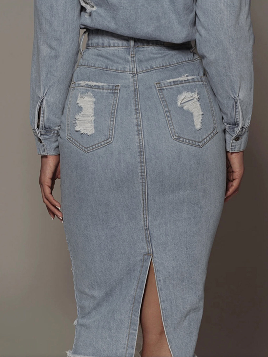 Light wash distressed slit denim skirt from Trendsi, featuring frayed edges and a high slit for a casual, trendy look.