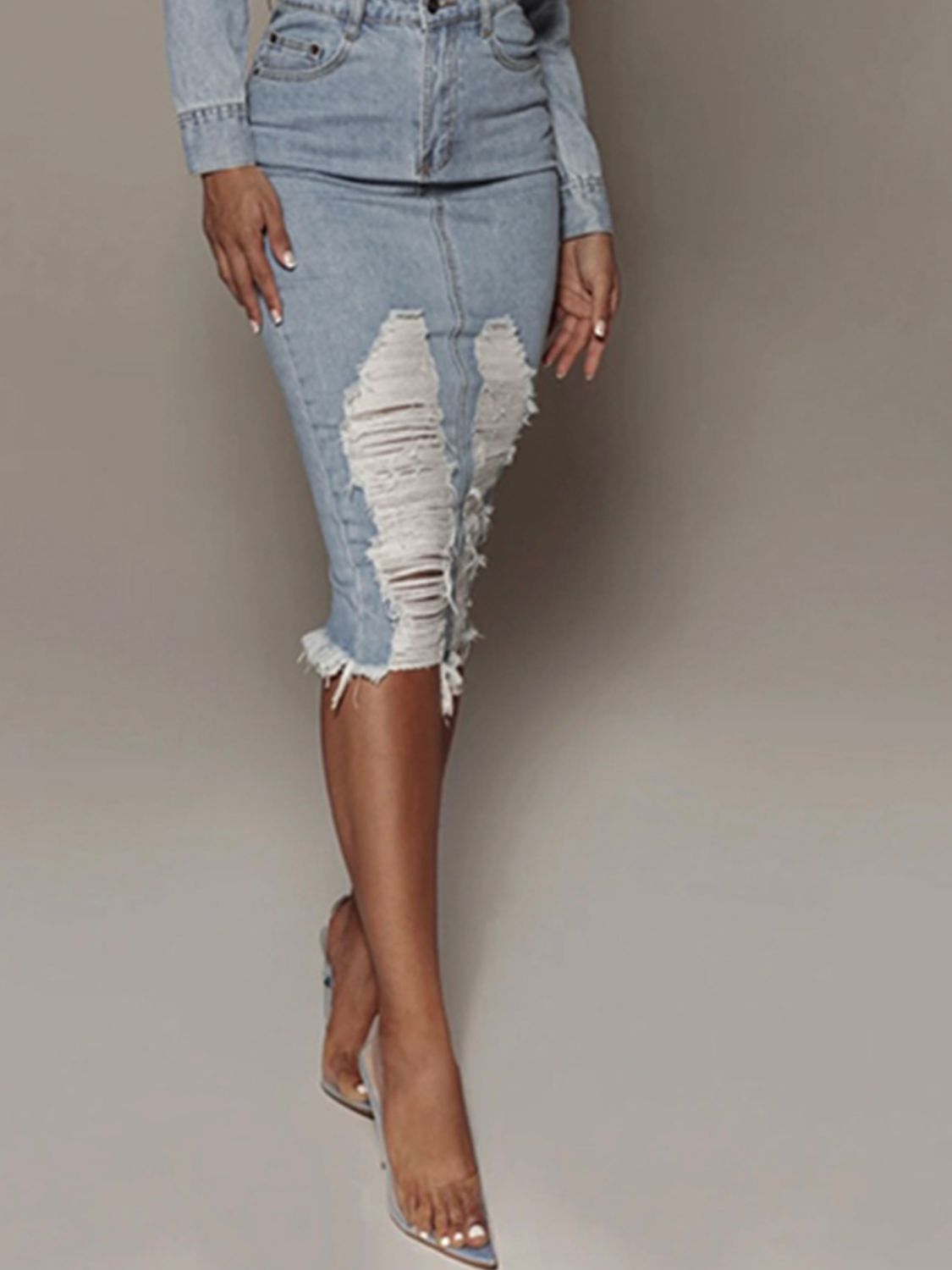 Light wash distressed slit denim skirt by Trendsi, featuring frayed edges and a high-waisted fit, worn with casual top.